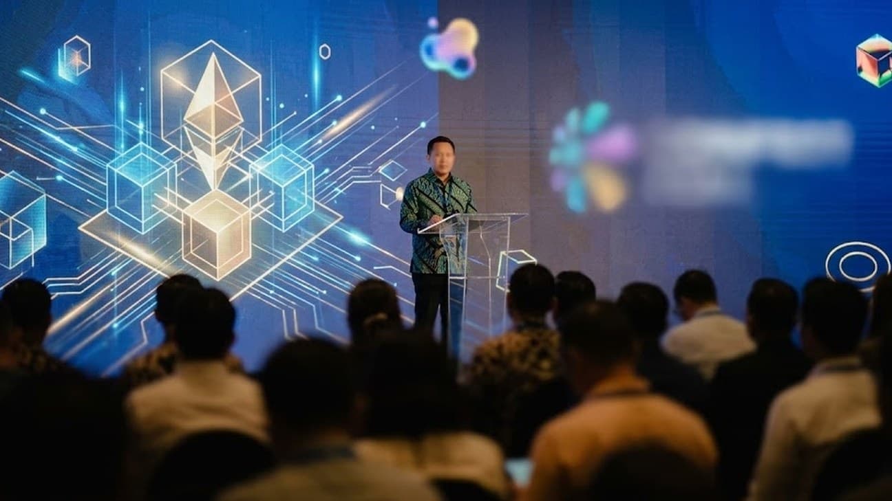 A regulator addresses a conference audience from a lectern, a large digital screen behind them, seen from the back of the room.