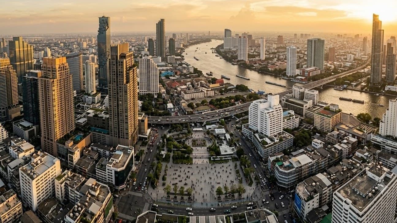 Aerial overhead view of a dense financial-district grid of high-rise towers around a bay at golden hour, city blocks and a river bend below